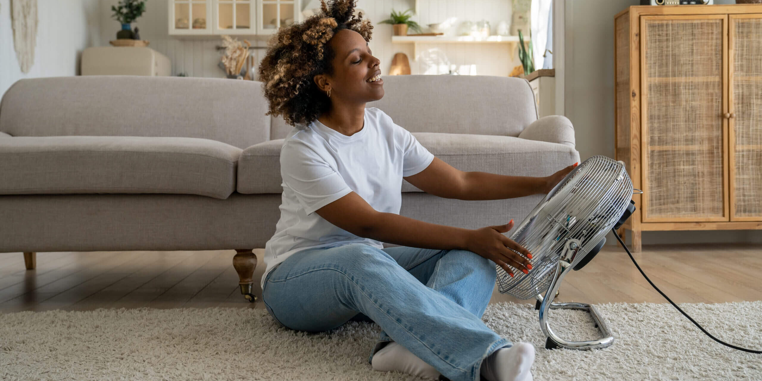 Satisfied happy young African American woman using fan at home during extreme summer heat