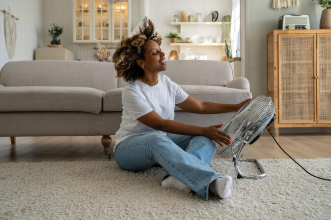Satisfied happy young African American woman using fan at home during extreme summer heat