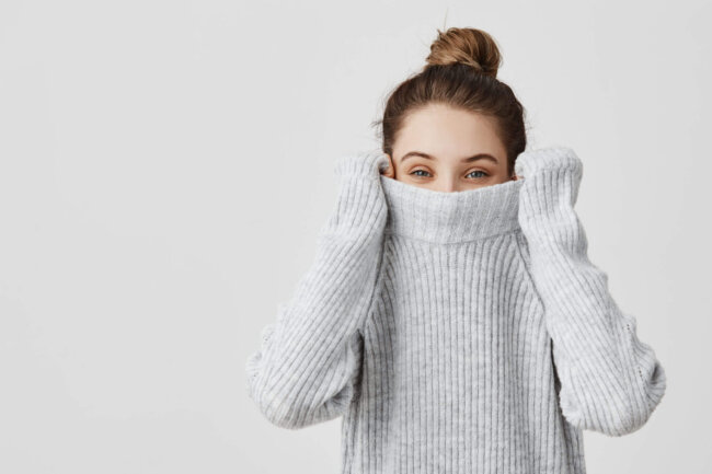 Portrait of girl pulling her trendy sweater over head having fun. Woman with tied hair in topknot being childish disappearing in her clothes looking from underneath. Happiness concept